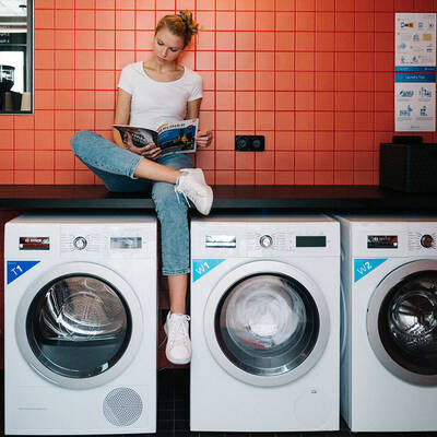 Junge Frau sitzt auf Waschmaschine in der Waschküche des Stayery Berlin Friedrichshain